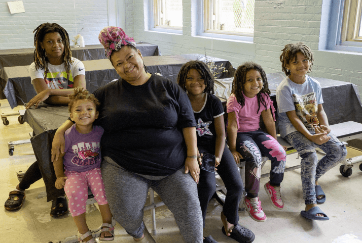 A caregiver seated with five smiling children at a community meal program