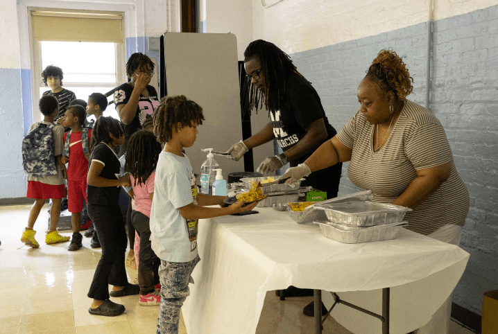 Volunteers serving hot meals to children lined up at a community center